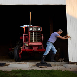 Man opening a barn door with an old red tractor inside wearing chore boots
