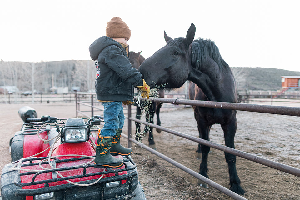 Child feeding horse standing on ATV wearing Kids Element Muck Boots
