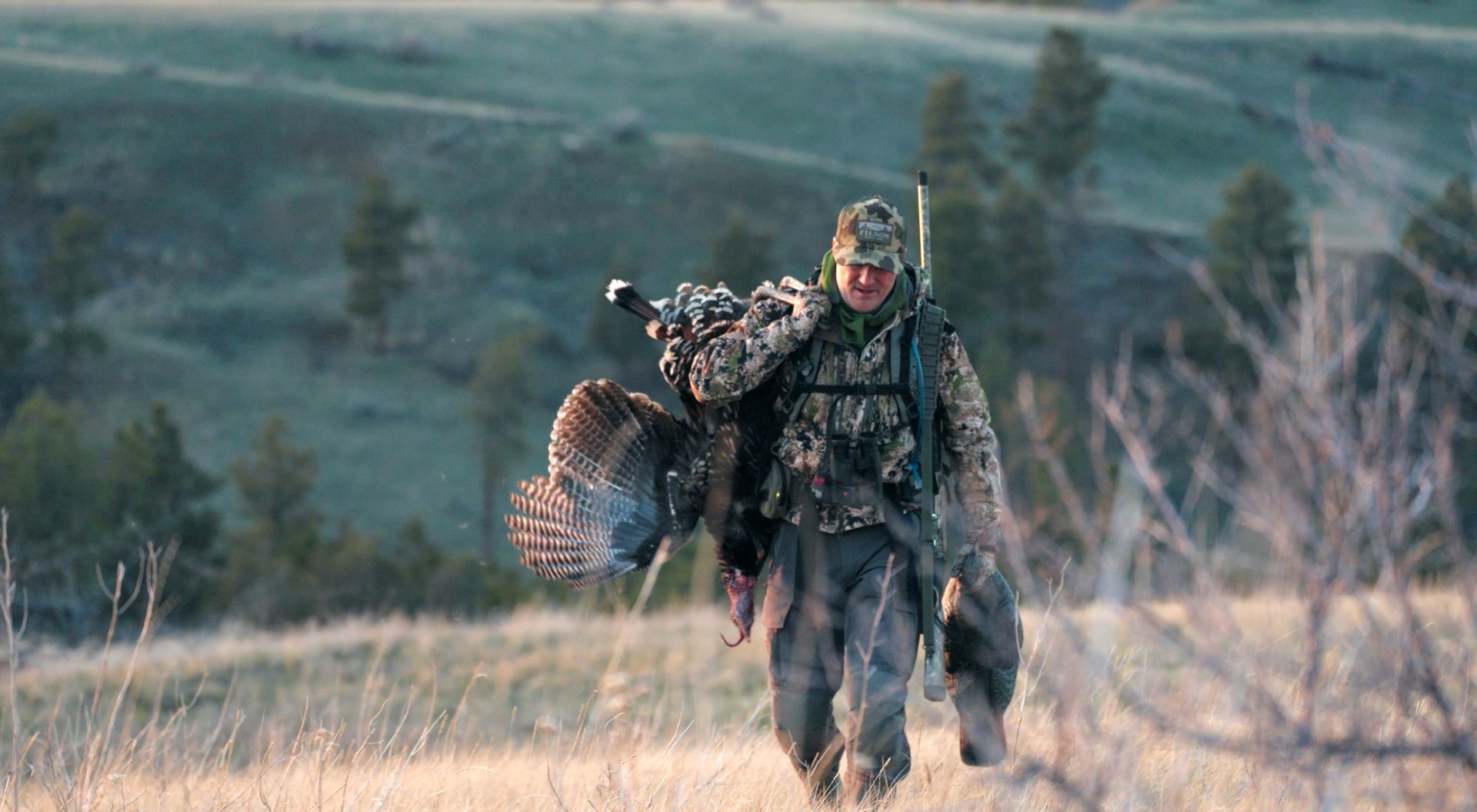 Jody Marler in camouflage walking through a field with a turkey on a leash.
