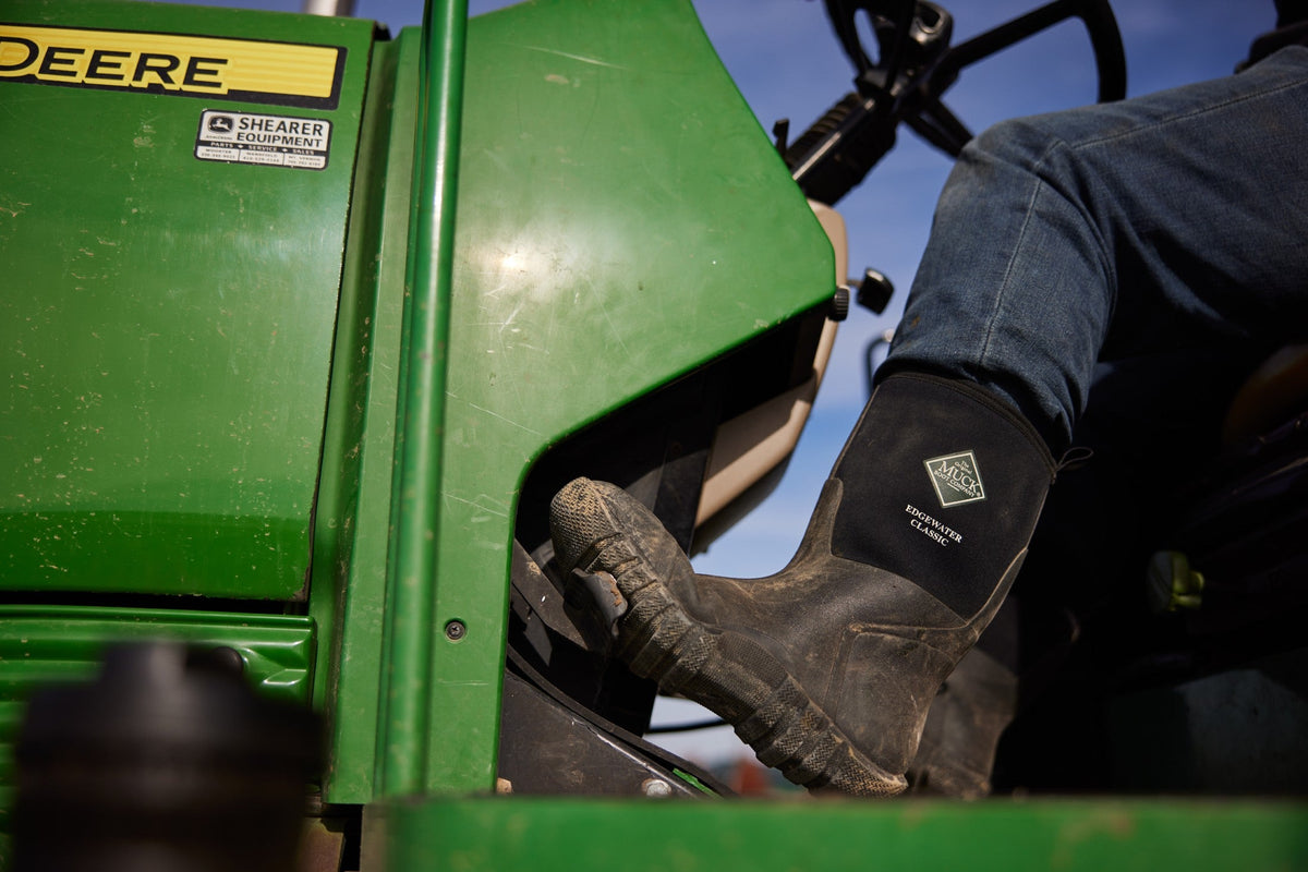Farmer in black boots with foot on the pedal of a green tractor