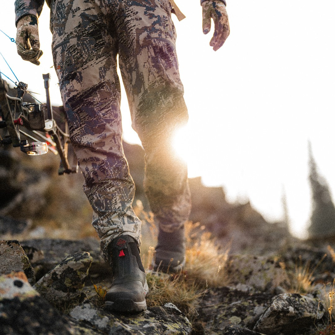 Man dressed in camo walking across rugged terrain at sunrise