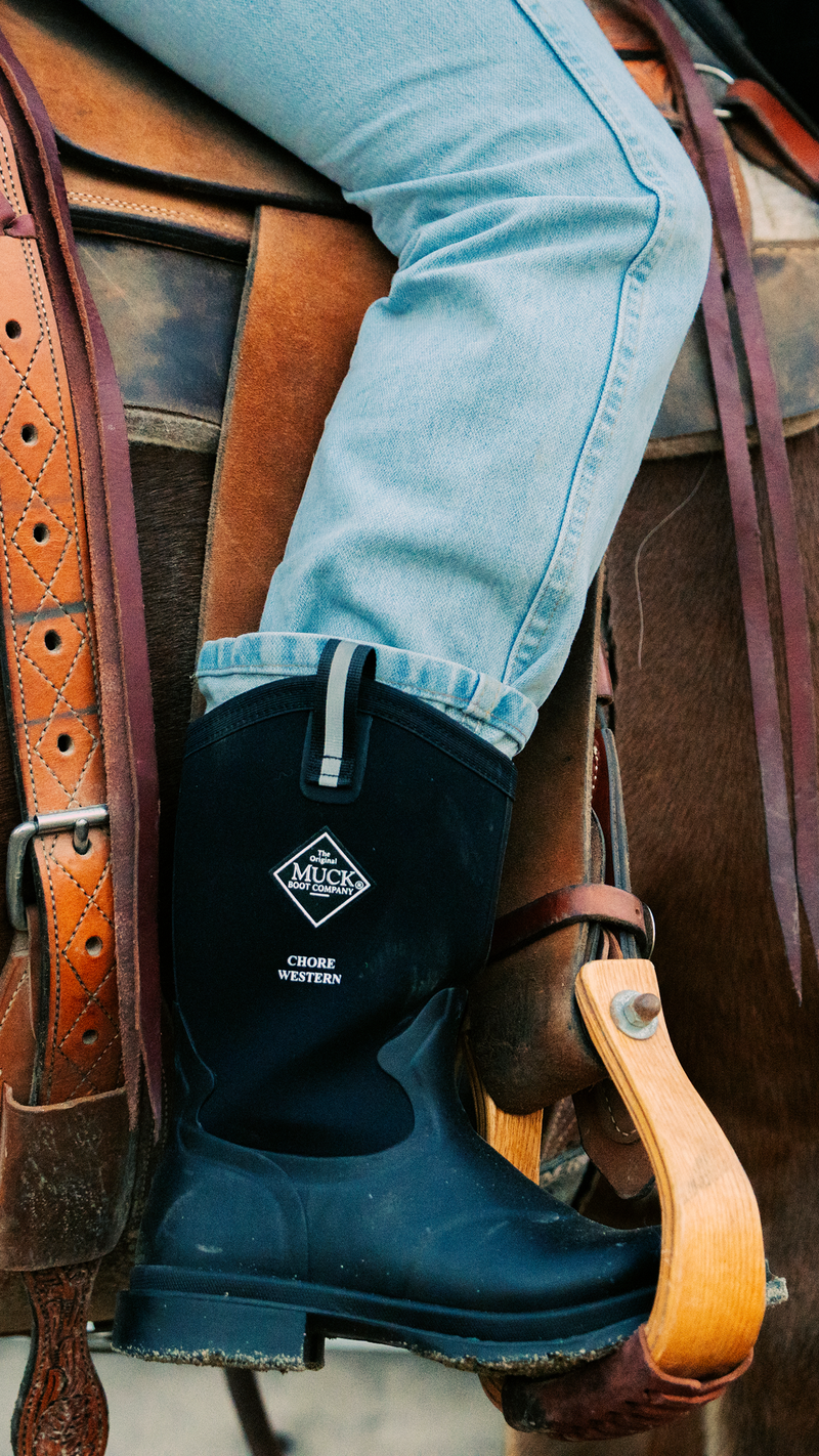Person wearing black Muck boots on a horse saddle