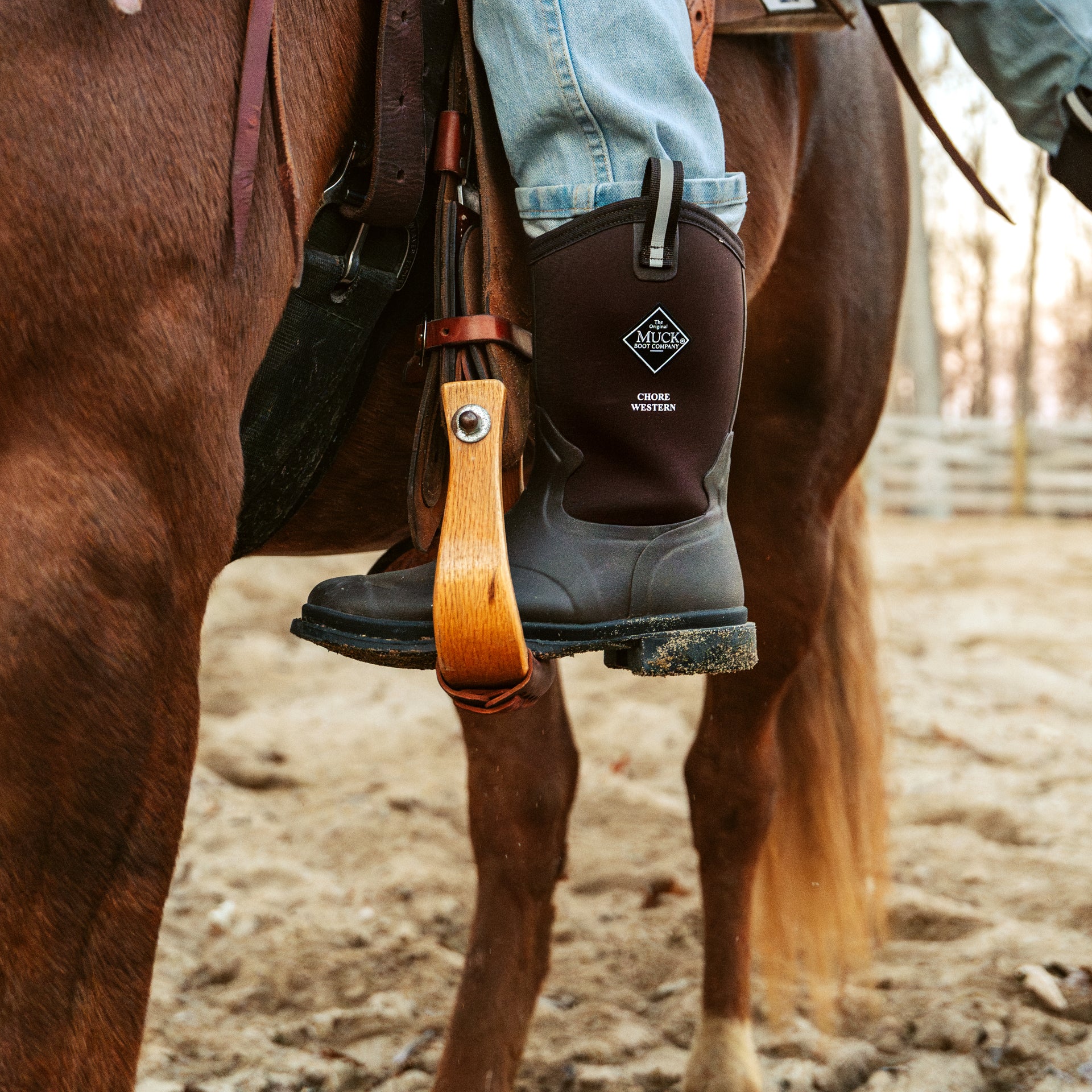 Person wearing a brown chore boots with a visible brand logo, climbing into a saddle.