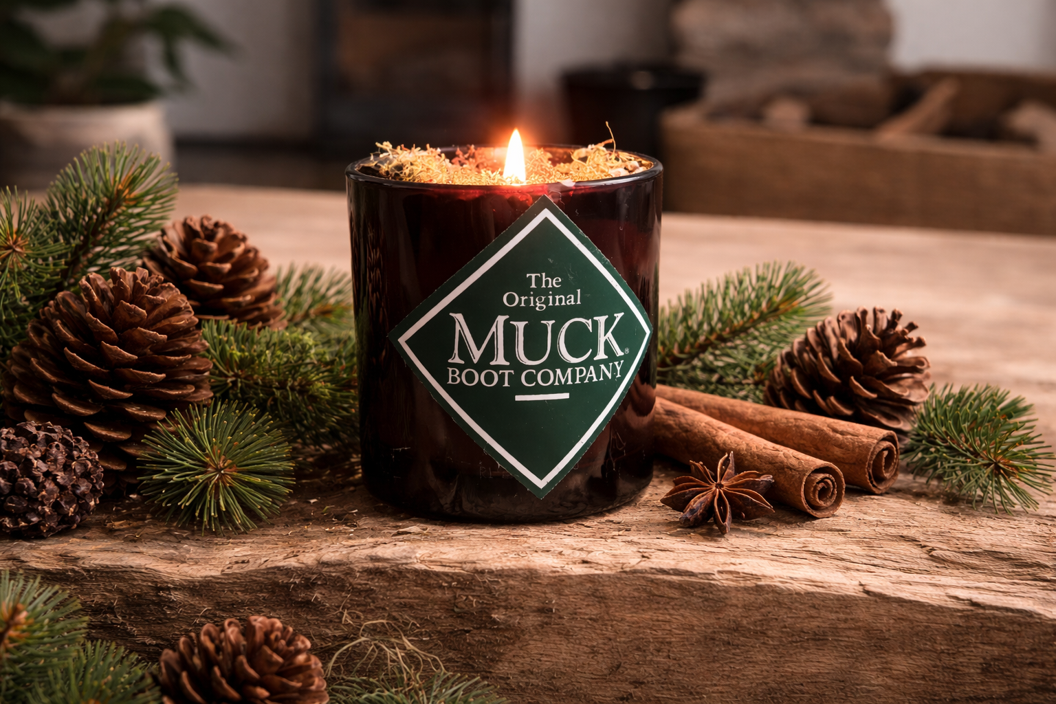 Muck Boot Company candle on a wooden surface with pine cones and cinnamon sticks