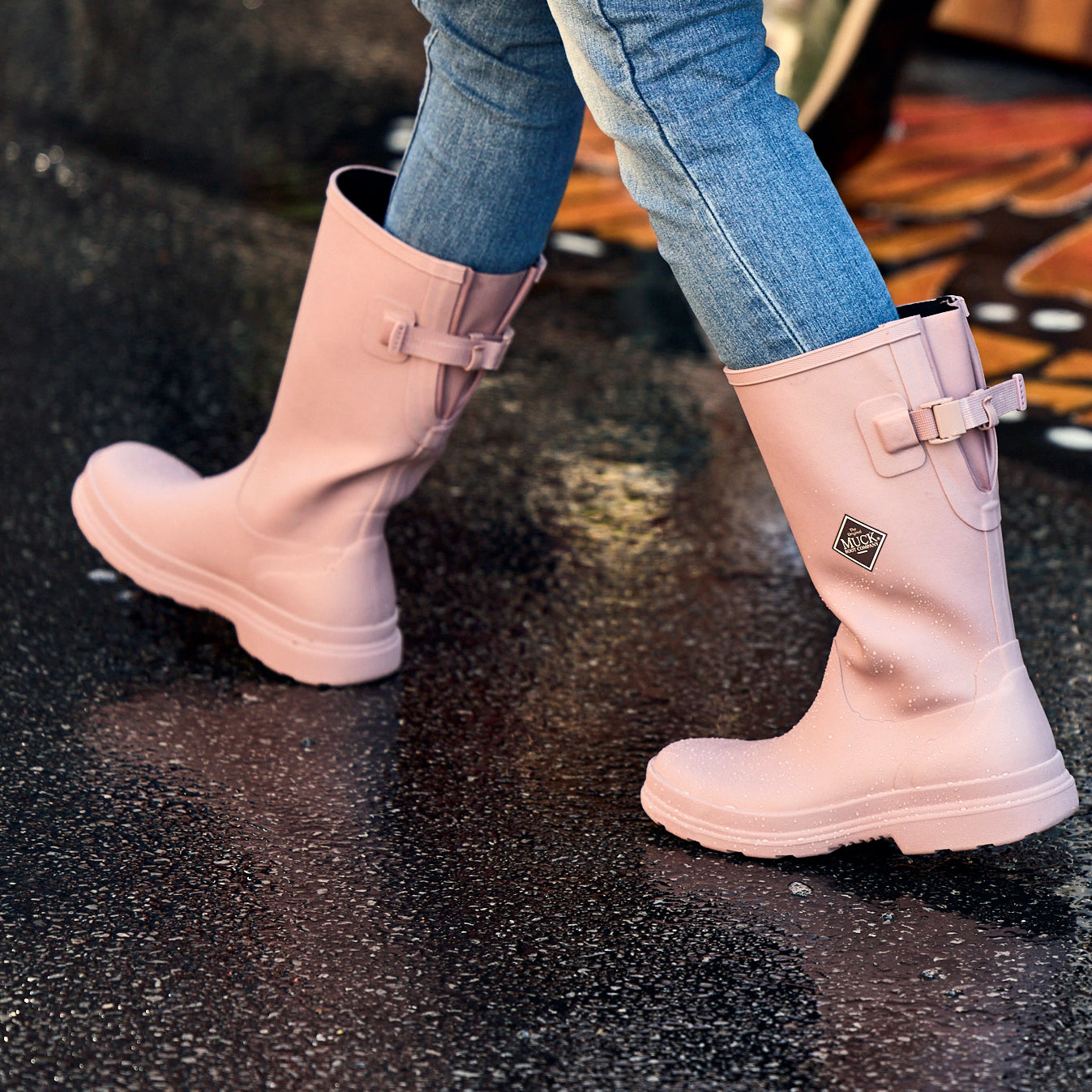 Pink rain boots worn with blue jeans on a wet pavement