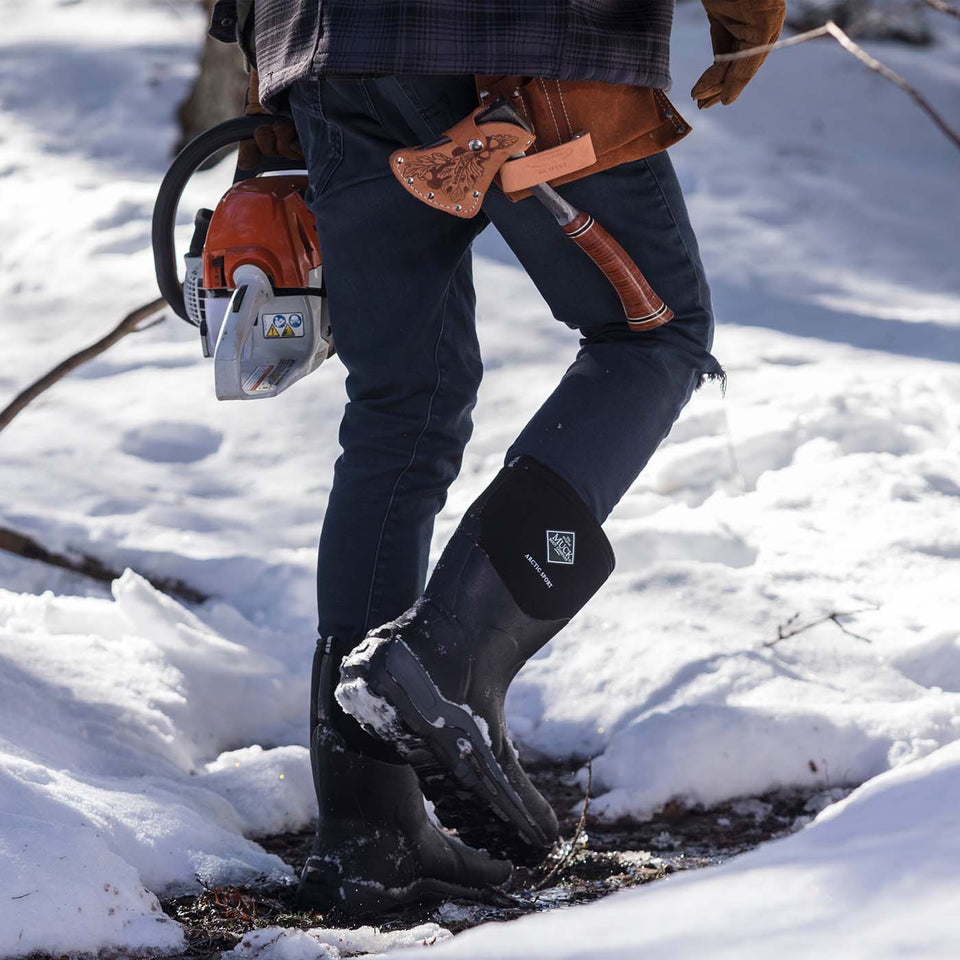 Person wearing black rubber boots with a chainsaw in a snowy environment