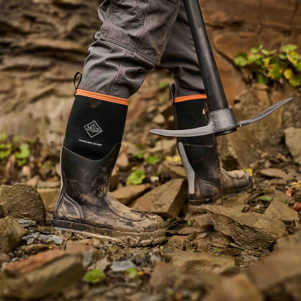 Person wearing black rubber safety boots with orange accents on a rocky terrain