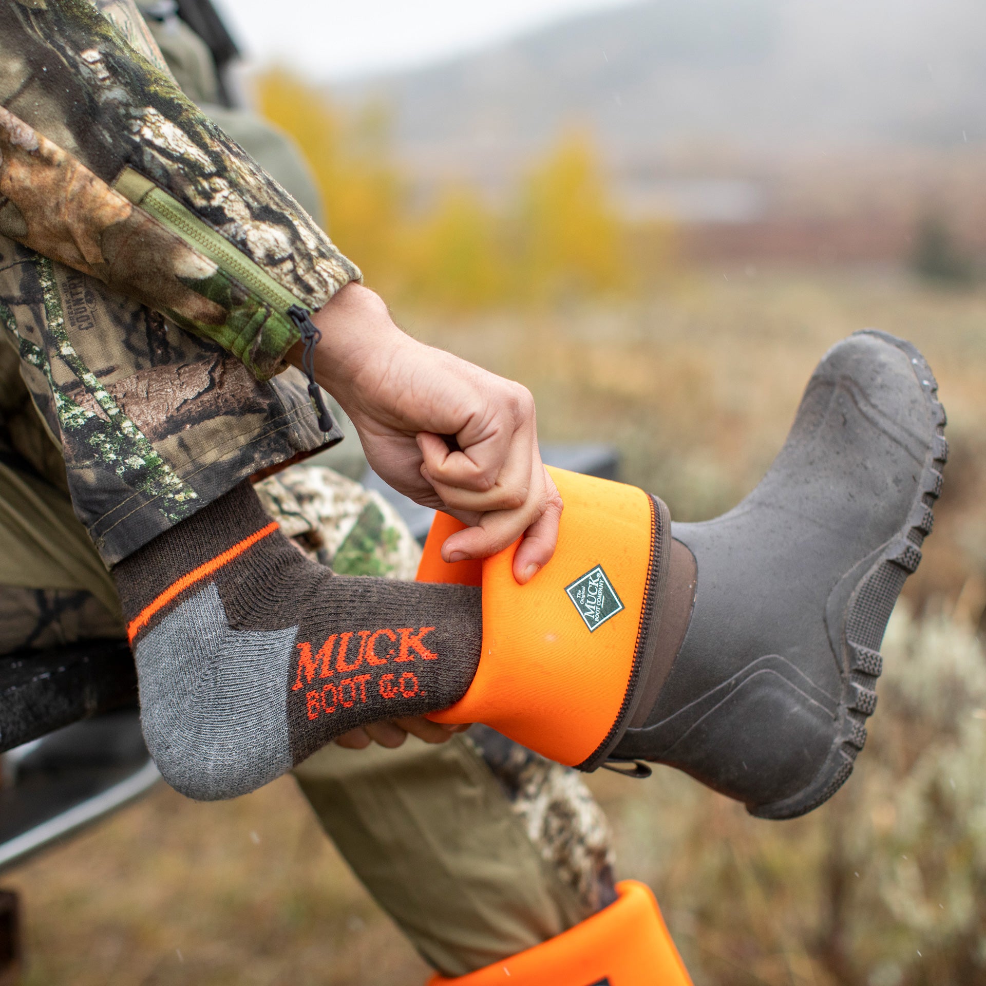 Person wearing Muck Boot Co. boots with orange accents in a natural setting