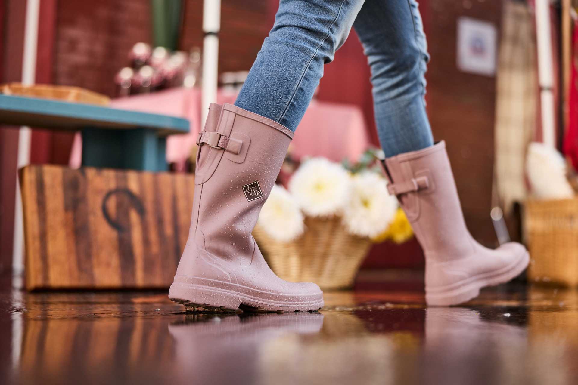Woman walking in pink woodrose tall adjustable rubber boots in a farmer's market setting.