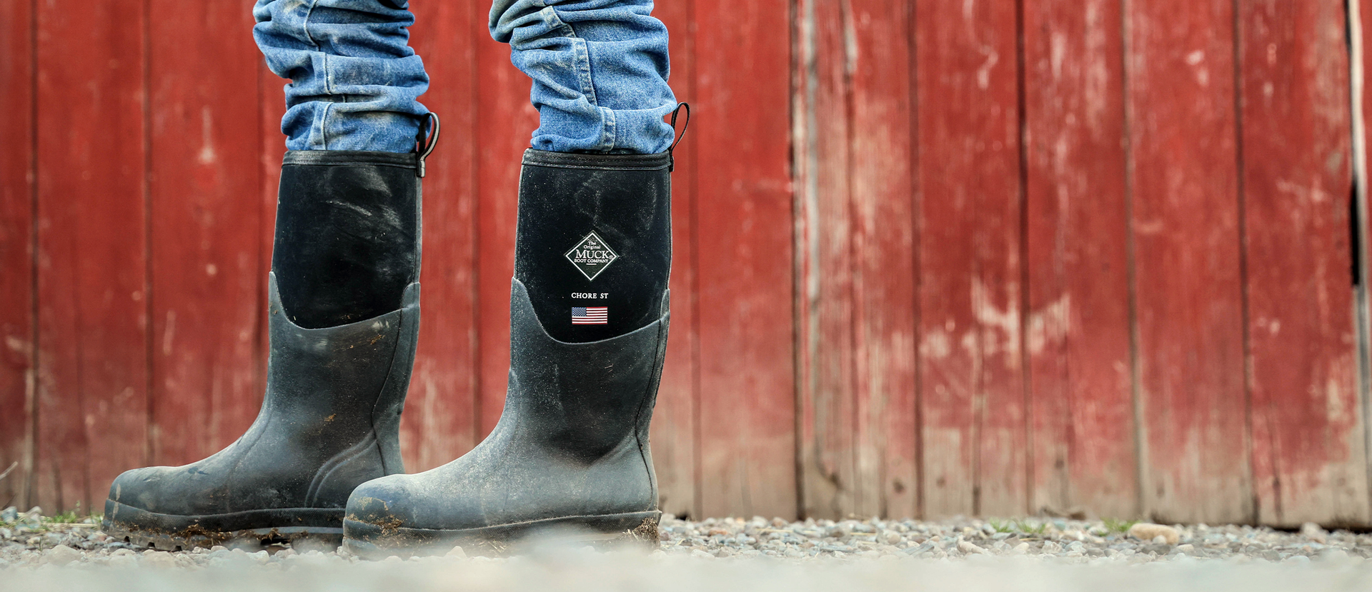 Chore Classic USA rubber boots with a Muck Boot Company logo worn by a person against a red wooden barn door.