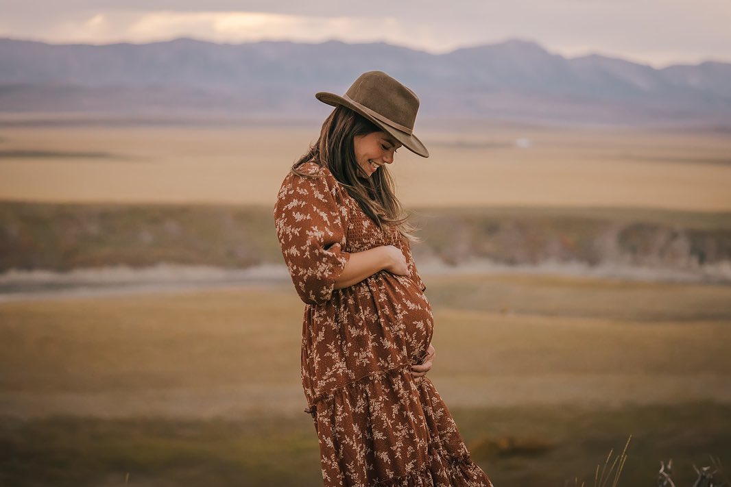 Abbagail McRuer in a patterned dress and hat standing in a field with mountains in the background