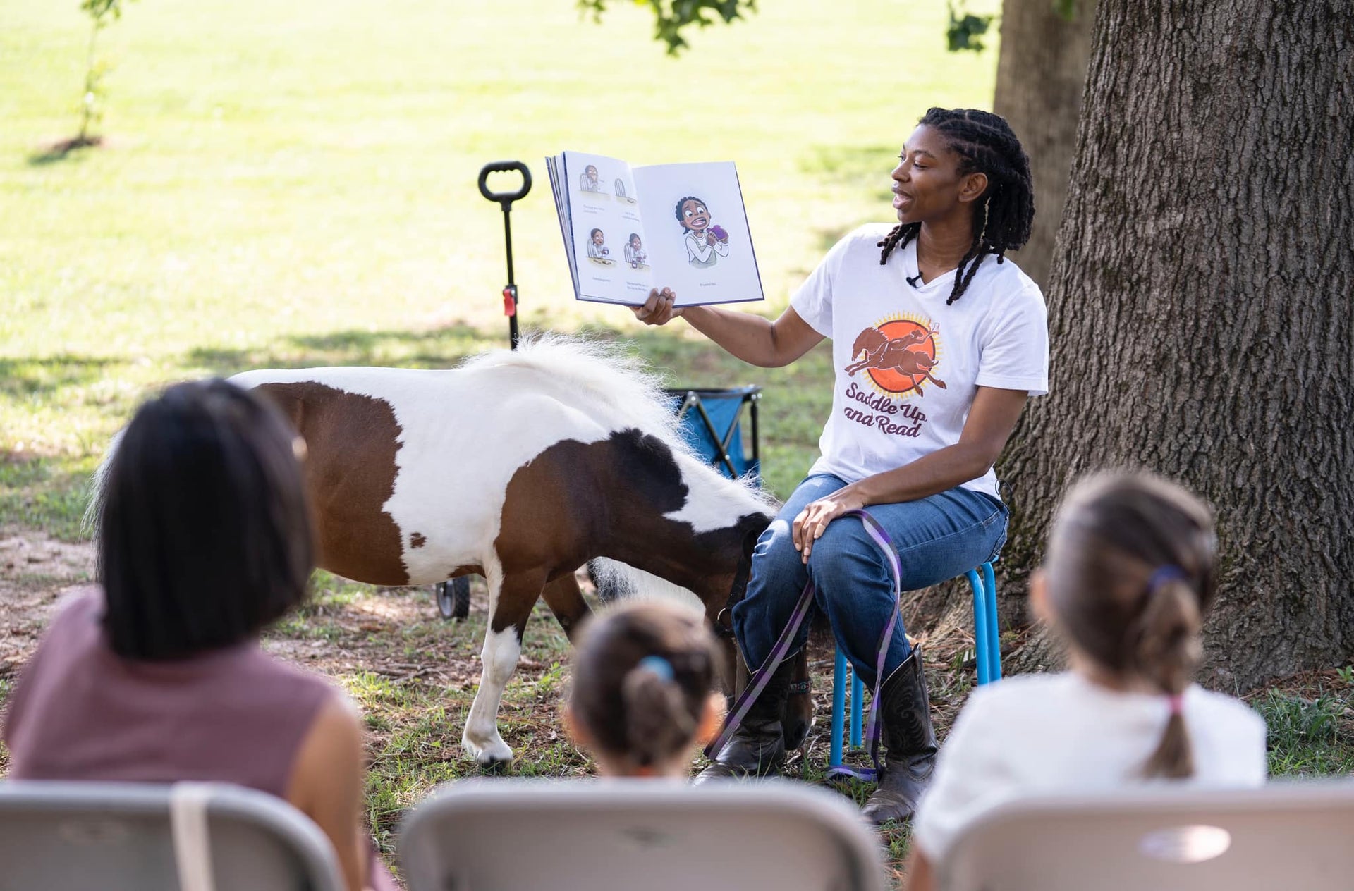 Caitlin Gooch reading to a group of children with a horse in a park setting