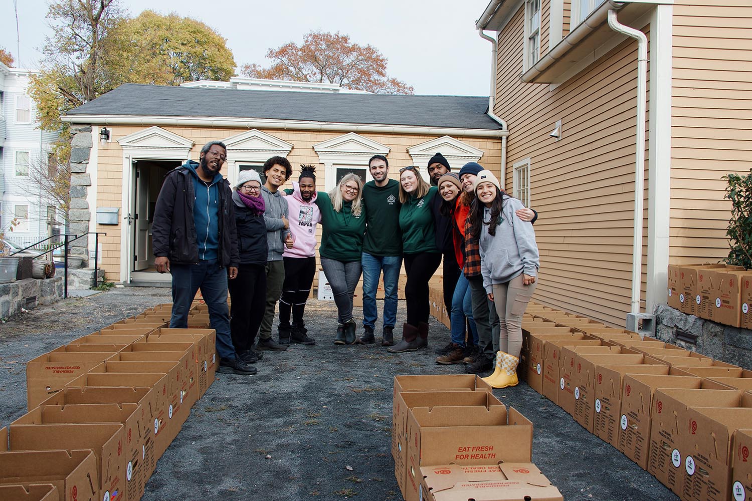 Group of people standing in front of a house with boxes, participating in a community service or donation event.