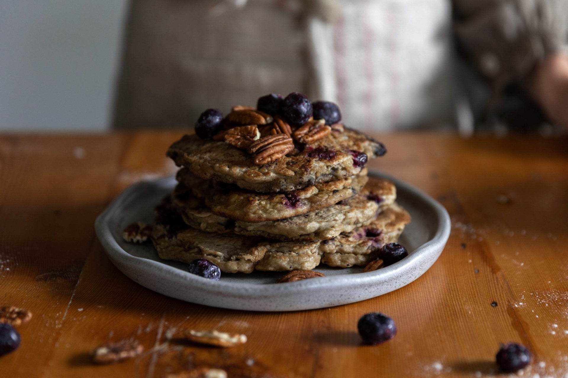 Stack of sourdough pancakes with blueberries and pecans on a plate, placed on a wooden table.