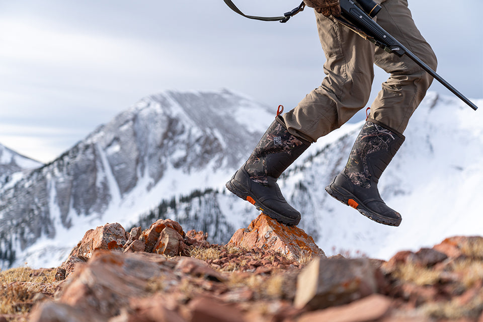 Hunter walking over rocky landscape wearing Muck Apex Pro Boots