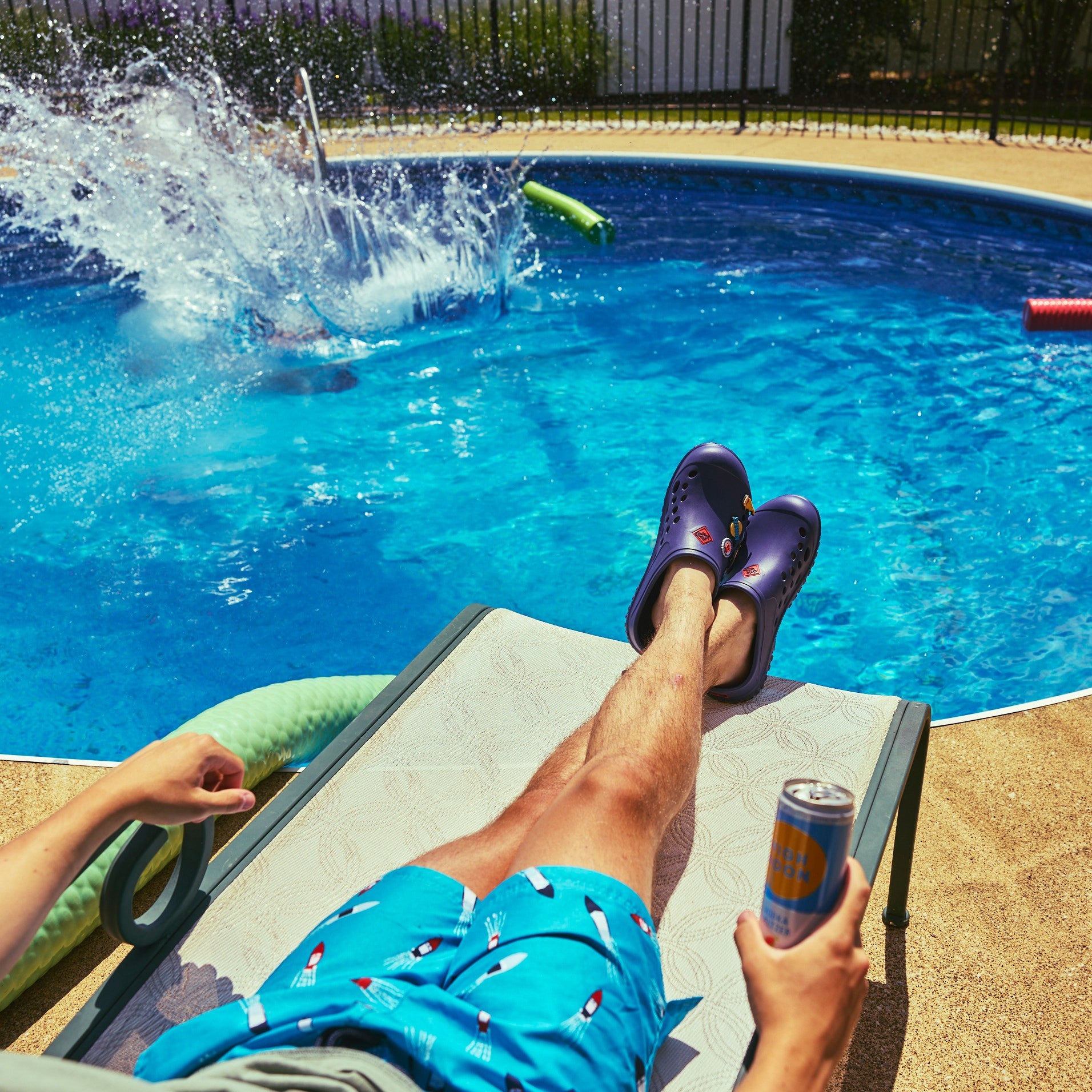 Barstool Sports - MLCMBS20 - Person lounging by a pool, splashing in the water, wearing muckster lite clogs with barstool sports insignia holding a can.