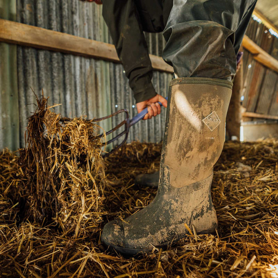 Person wearing muddy rubber chore boots in a barn setting