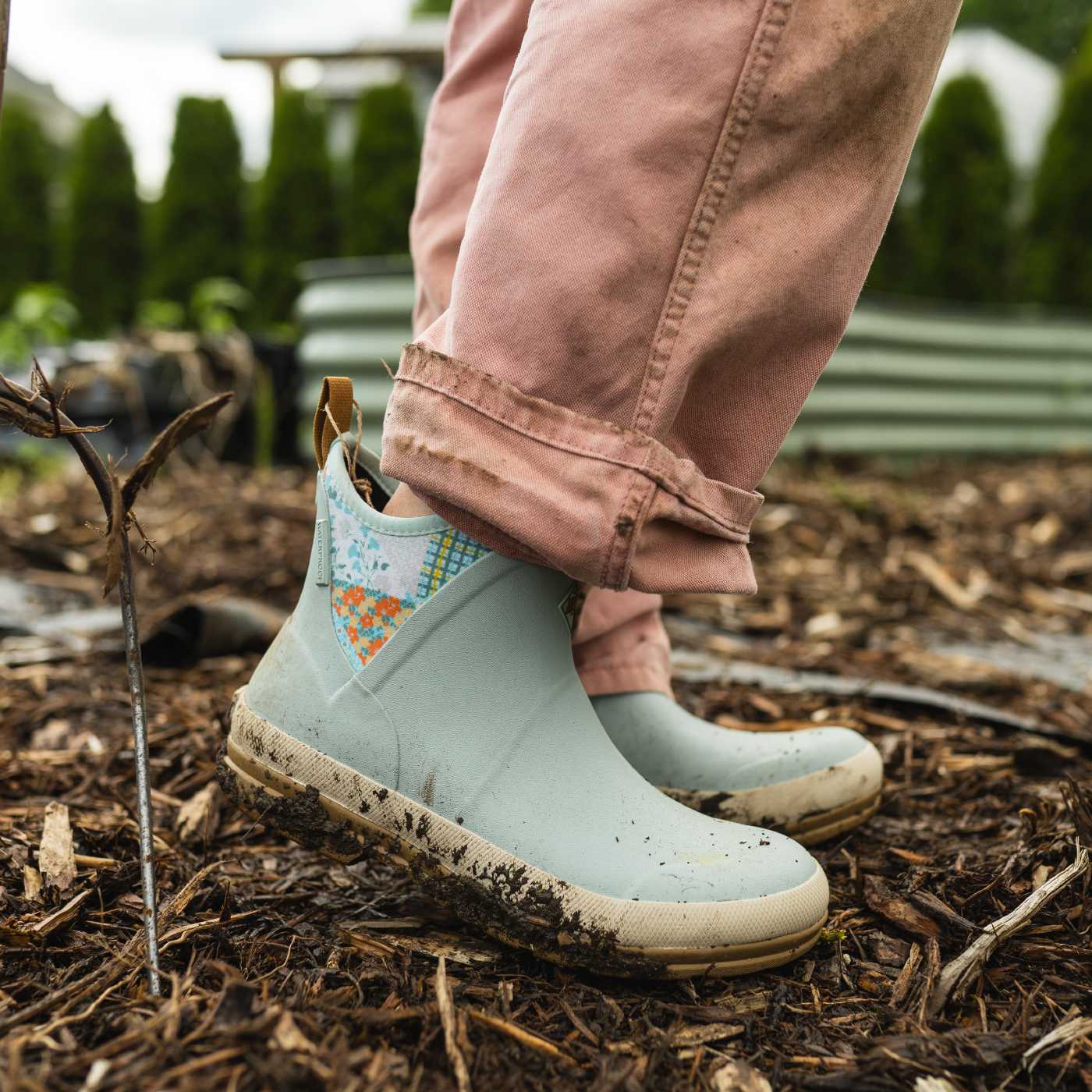Light blue rain boots with floral pattern worn by a person in a garden setting.