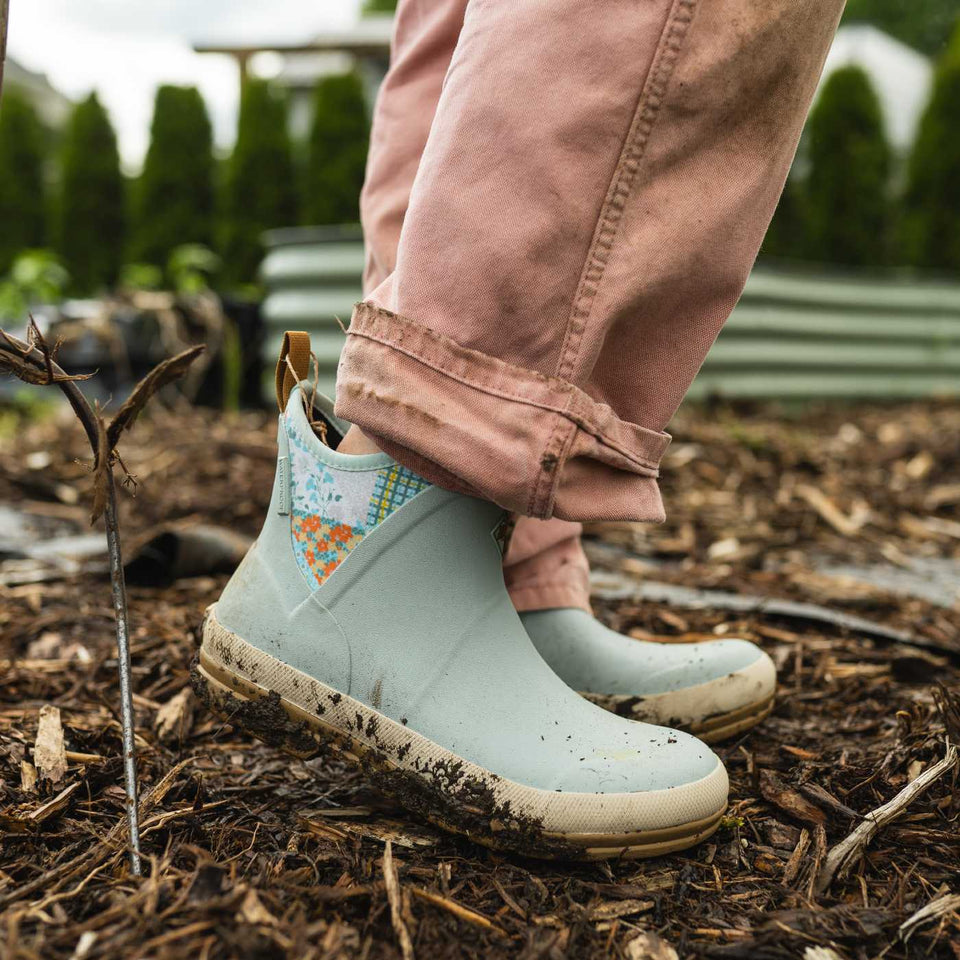 Light blue rain boots with floral pattern worn by a person in a garden setting.