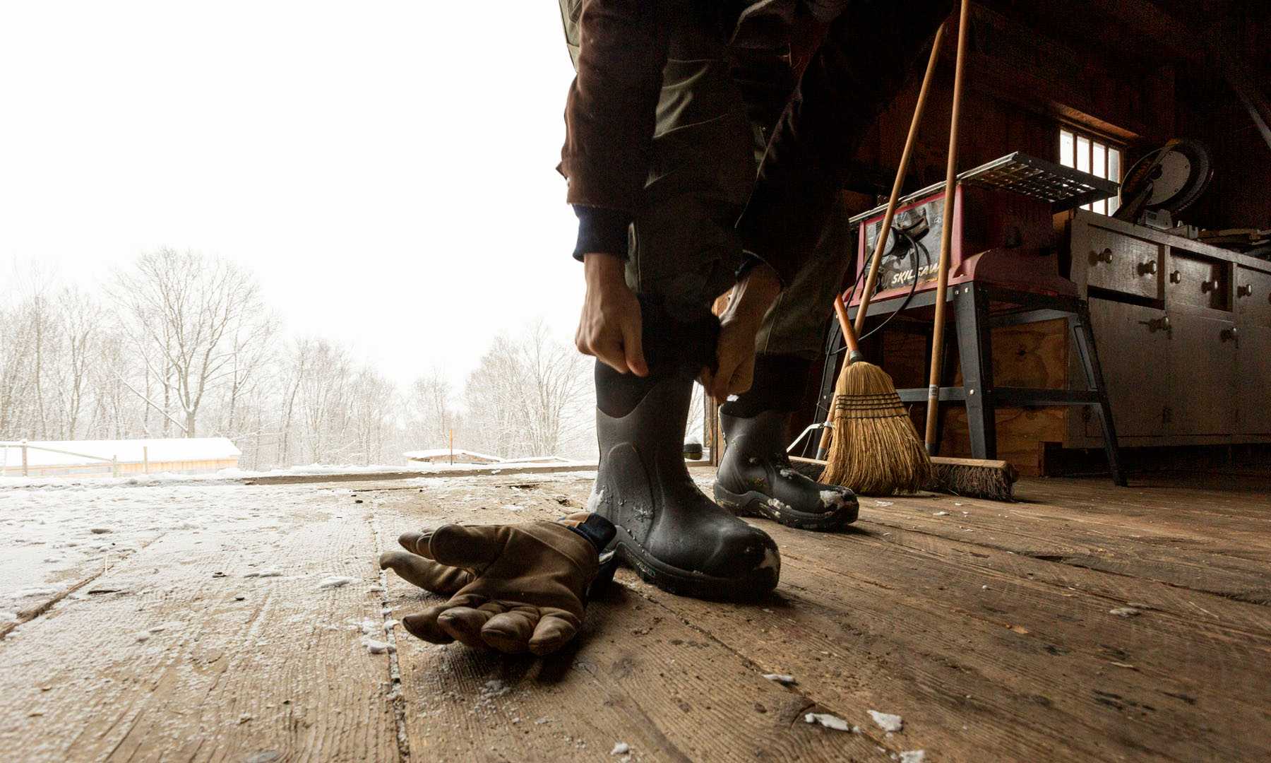 Person wearing rubber boots and gloves in a barn setting during winter storm