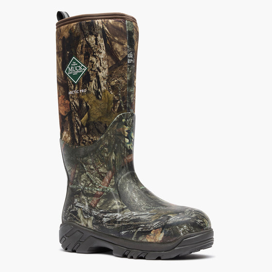 A single Muck Boots Arctic Pro boot with a realistic woodland camouflage pattern, featuring a dark gray rubber sole and a green and white Muck logo on the side, set against a plain white background.