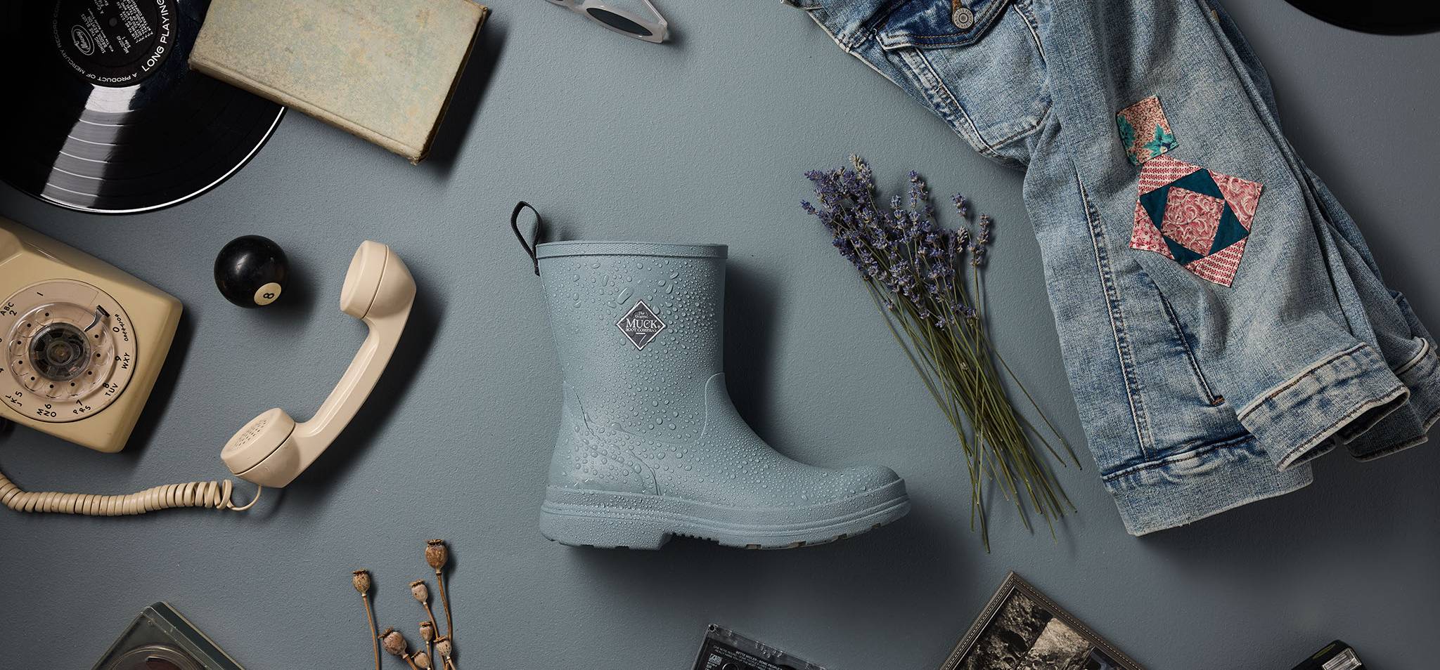 Blue waterproof rubber rain boot on a gray surface with various items around it