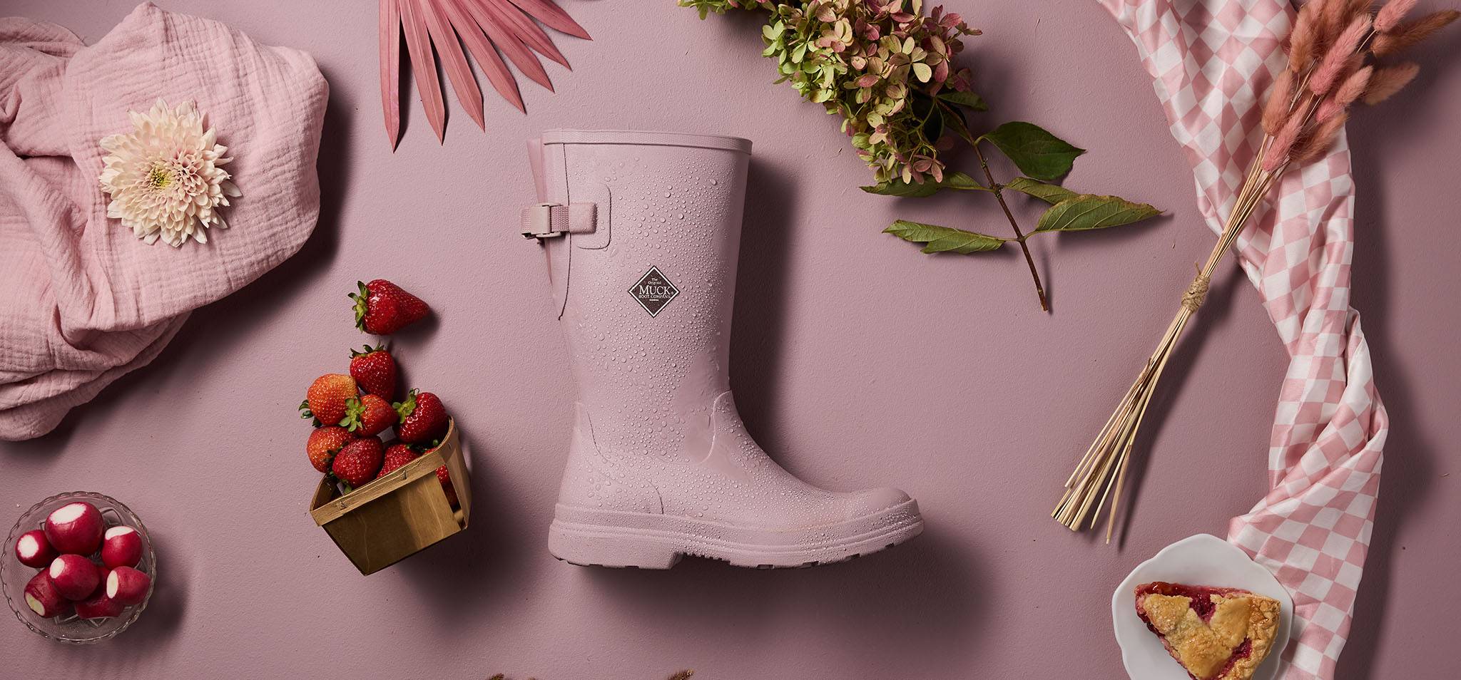Rainscape Woodrose pink rain boot on a pink background with decorative elements like flowers and berries.