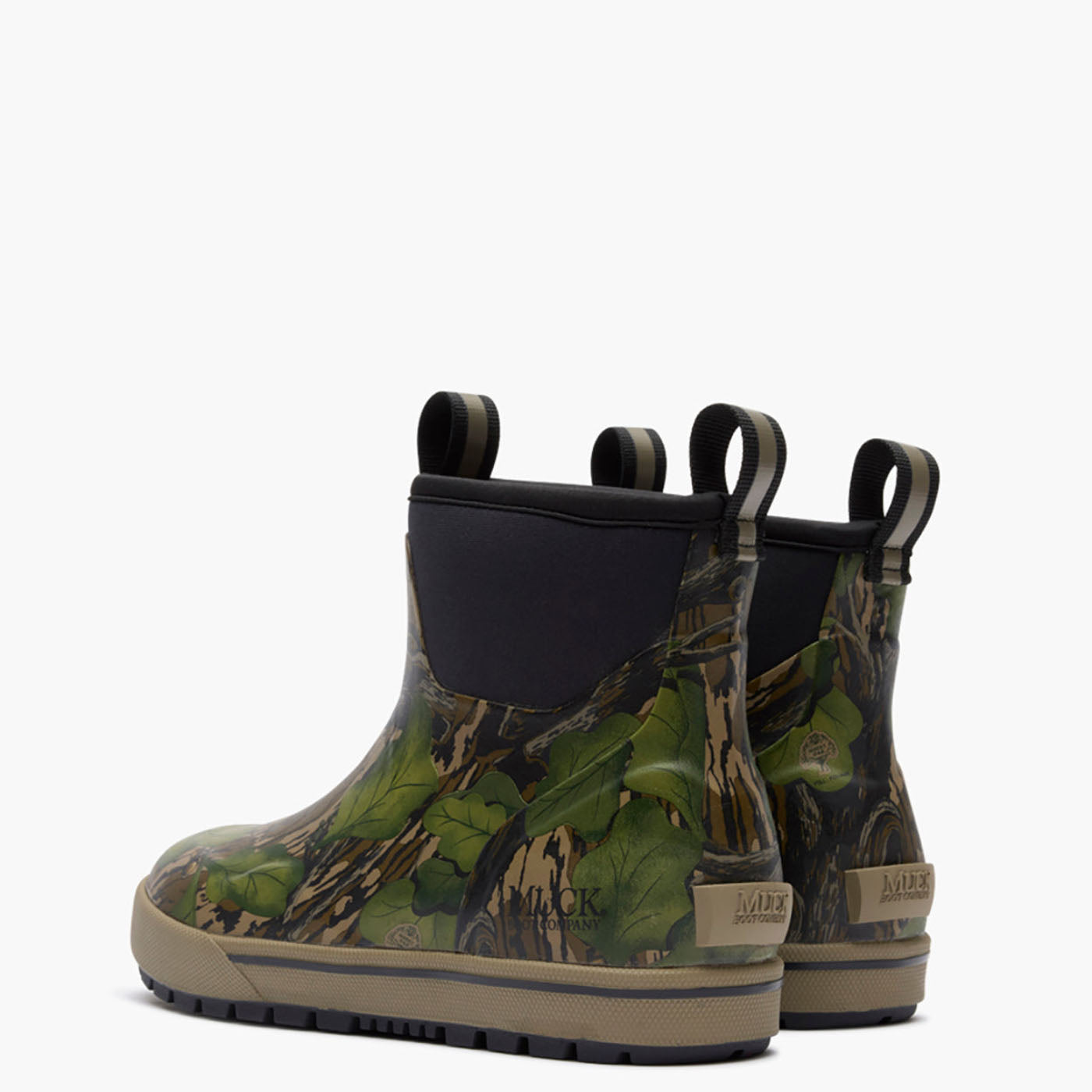 A pair of Muck boots featuring a green and brown woodland camouflage pattern, black elastic side panels, and tan soles, shown against a plain white background.