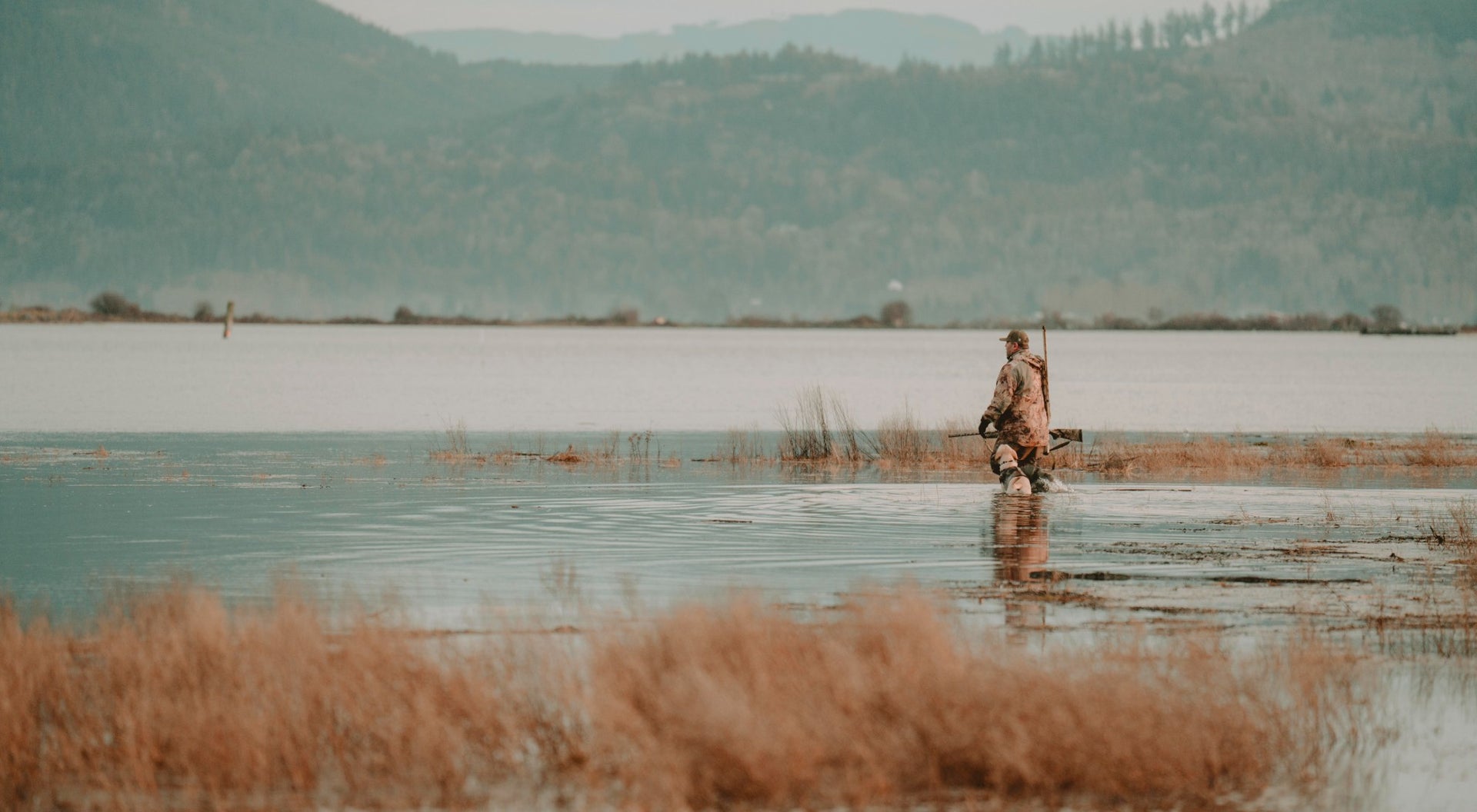 Man standing in knee high water holding his shotgun.